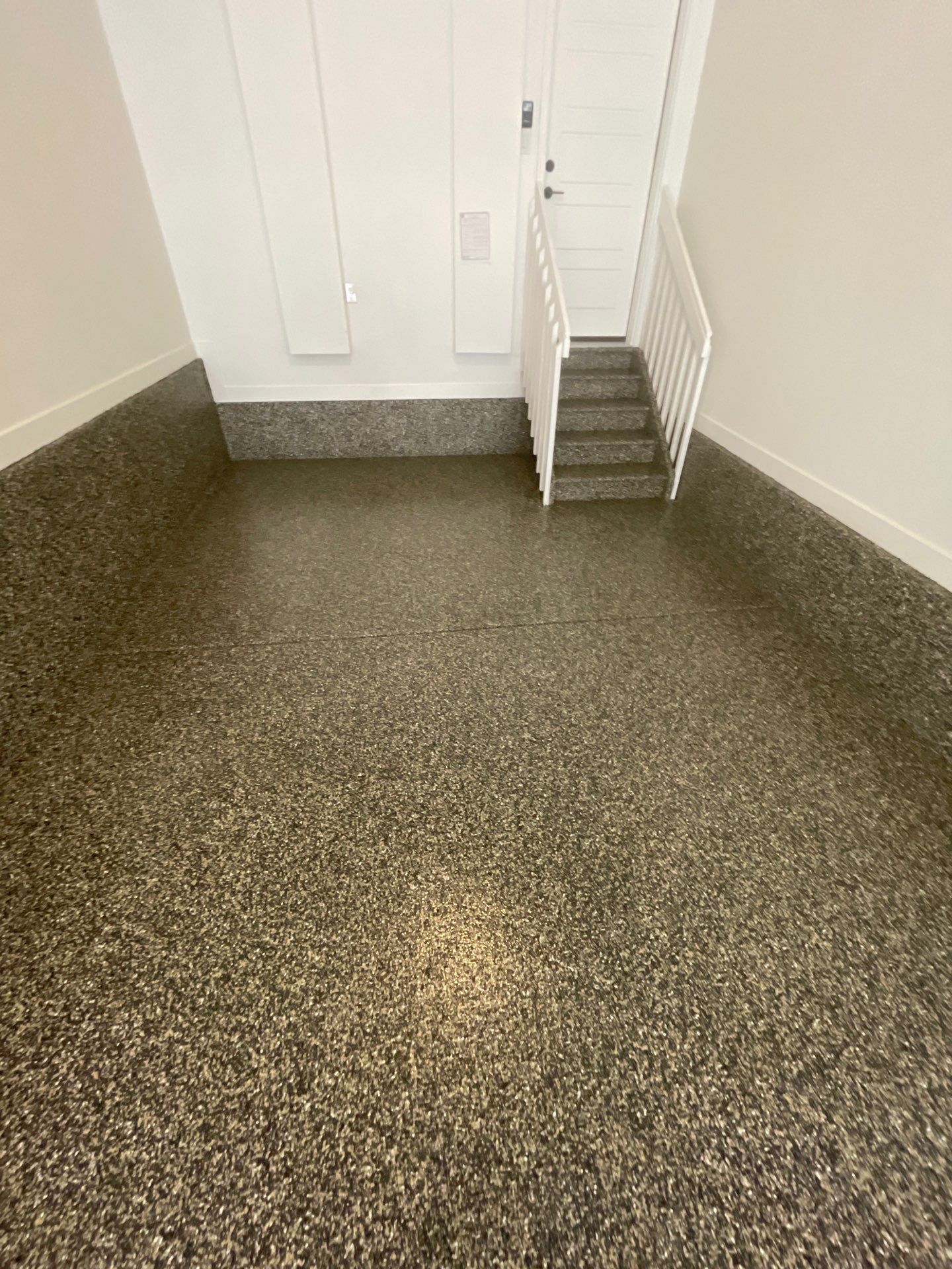 Small stairwell landing with speckled flooring, white walls, and a white door at the top of the stairs