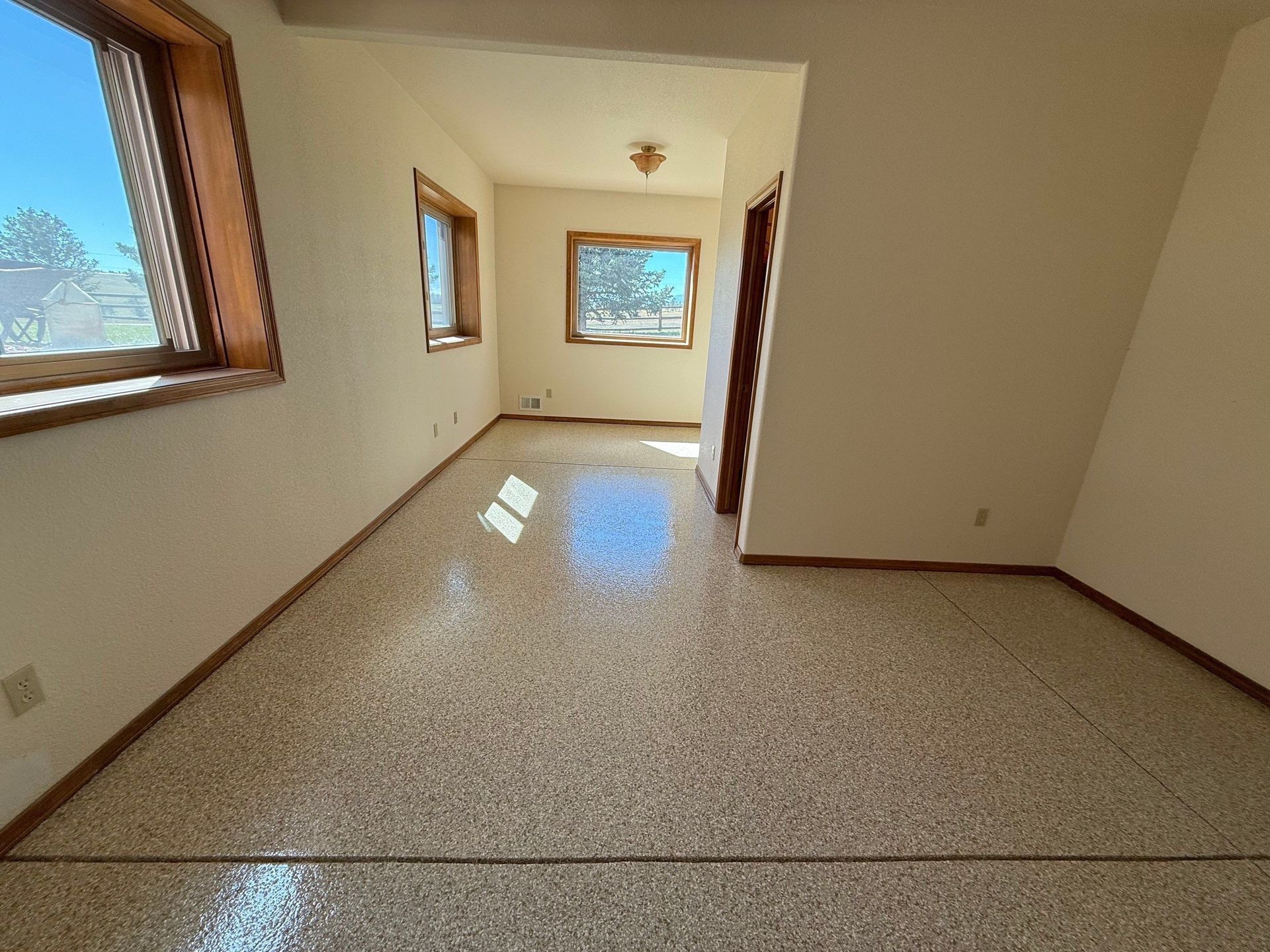 Empty beige room with tiled floor and several windows letting in natural light.