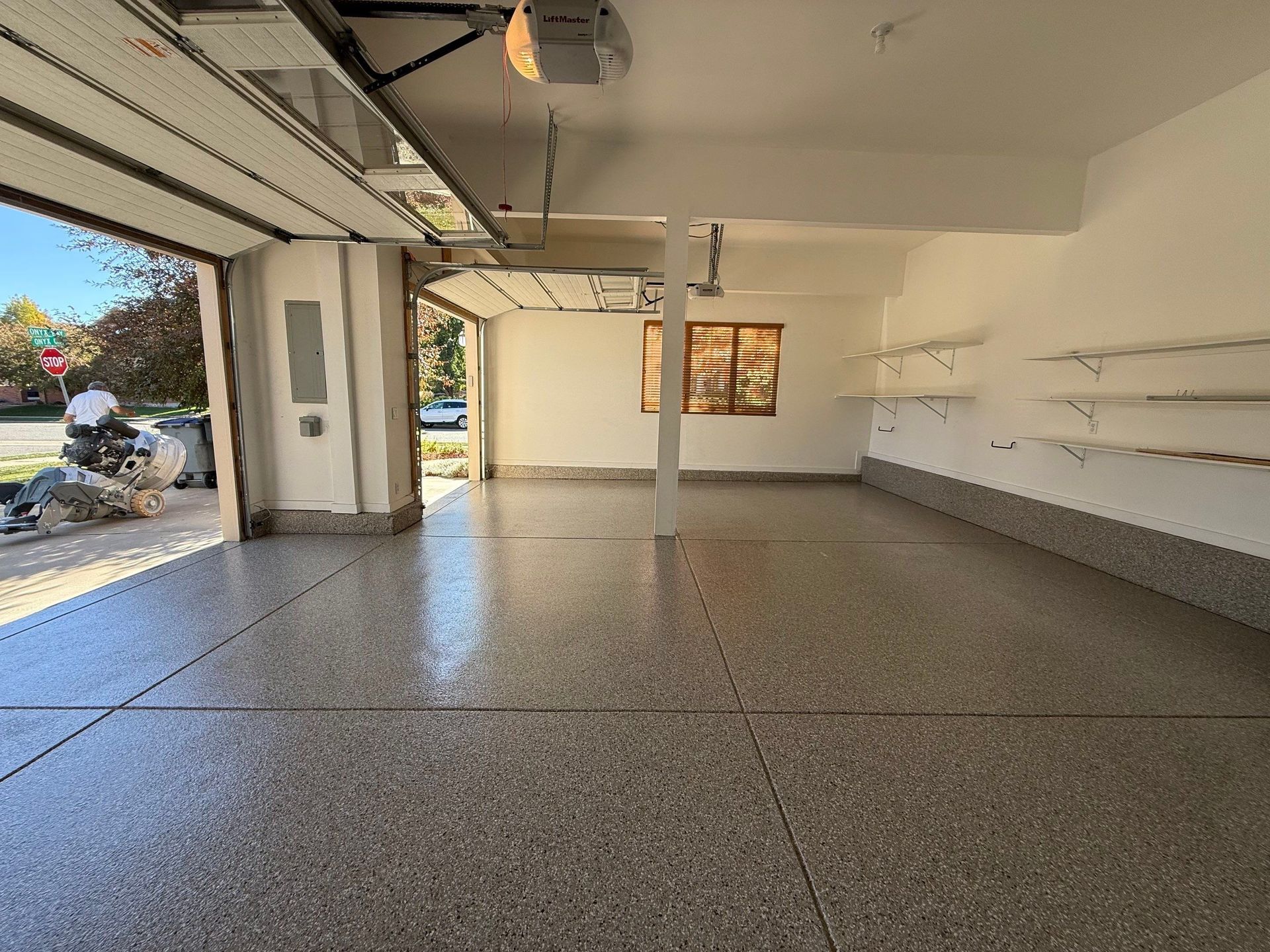 Empty garage interior with polished speckled floor, open door, wall shelves, and a hanging light.