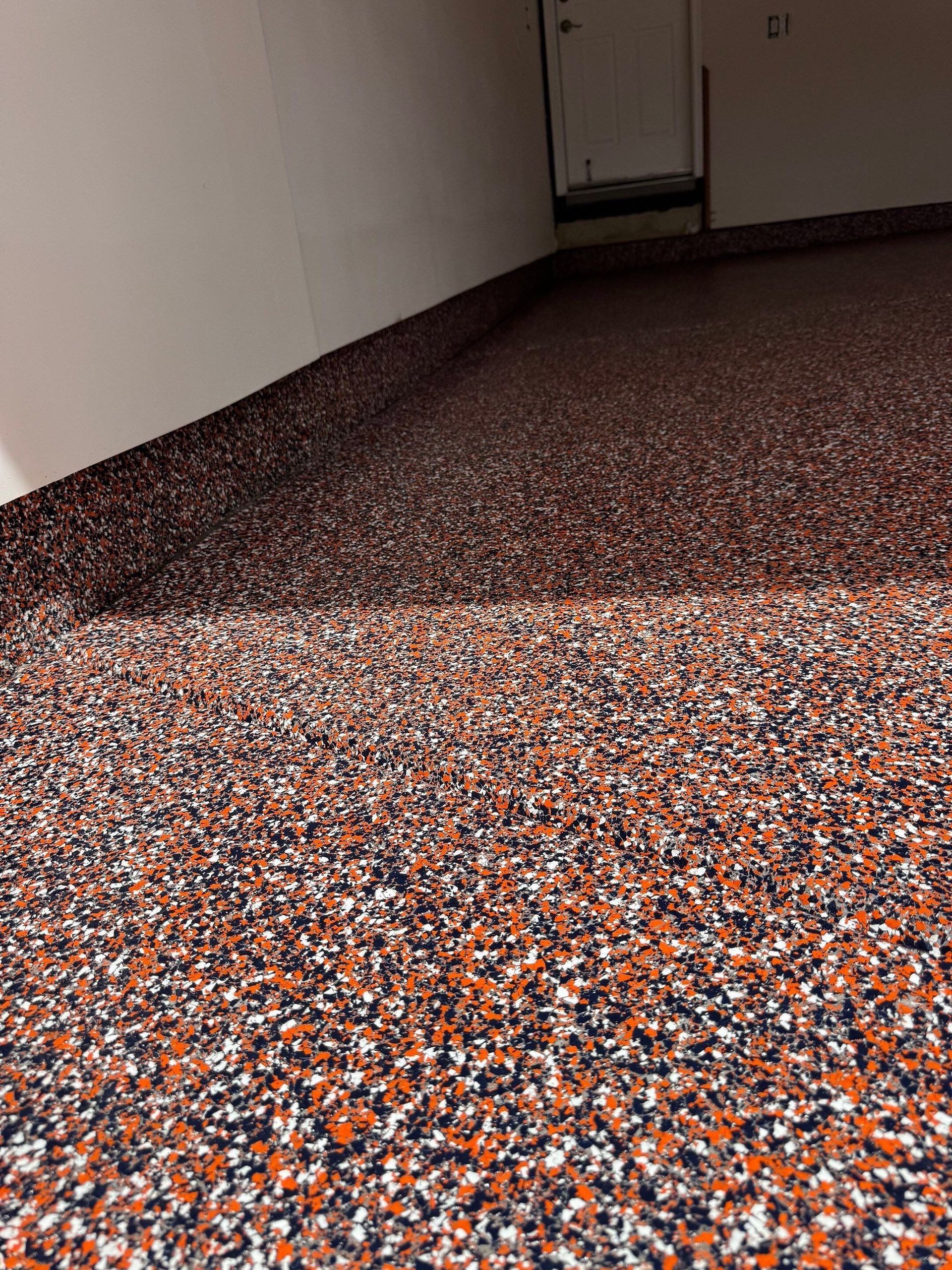 Textured orange, black, and white speckled floor in a narrow hallway with white walls.