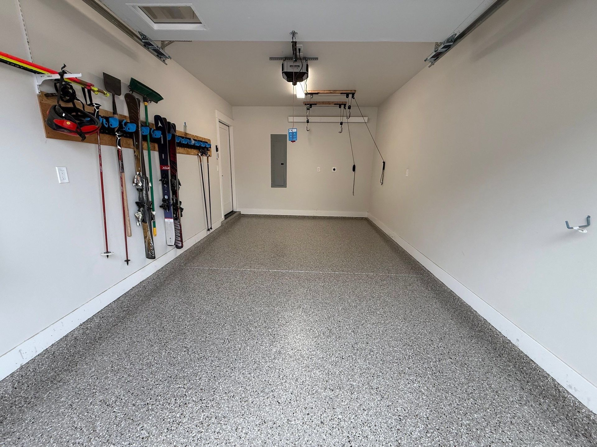 Empty garage with speckled floor, white walls, wall-mounted tools, and a closed back door.