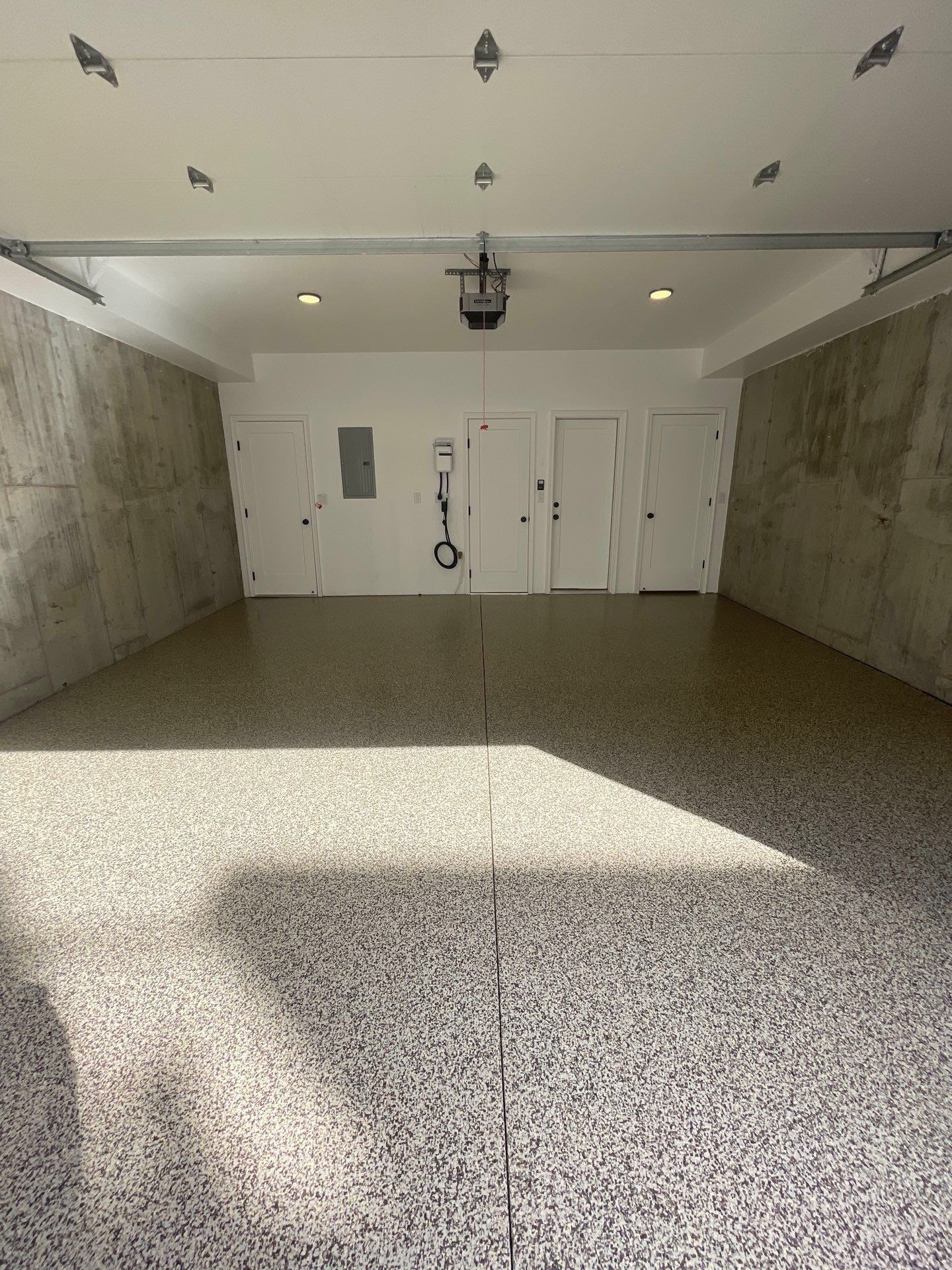 Empty garage with speckled floor, white doors, and sunlight casting shadows across the concrete.