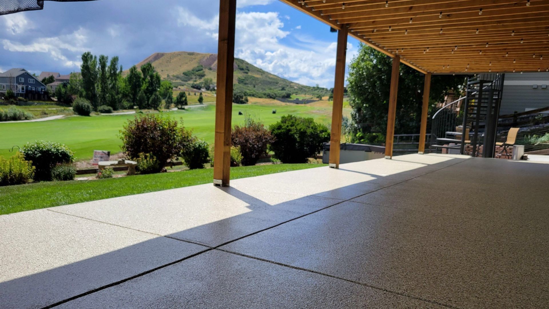 Covered patio overlooking a green lawn and hills, with wooden posts and stone flooring.