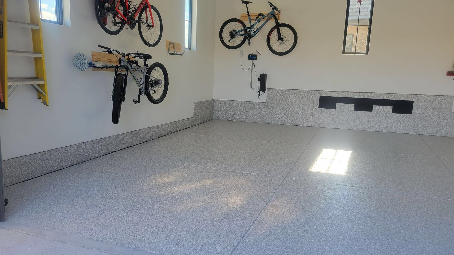 Garage wall with several bicycles mounted above a clean gray floor.