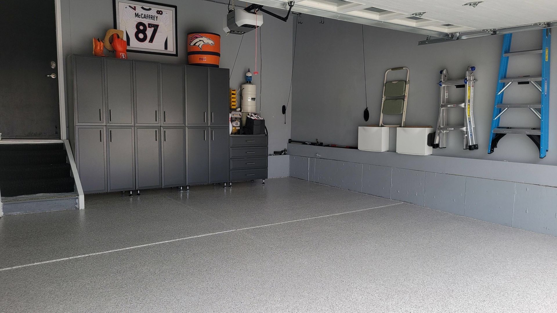 Gray garage interior with cabinets, shelves, a ladder, and a black dog on the left.