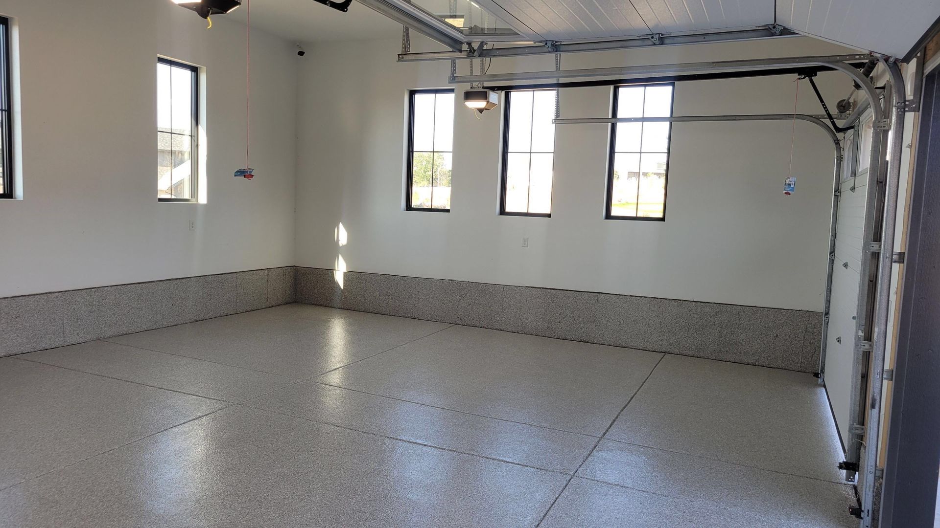 Empty garage interior with white walls, speckled floor, and several windows.