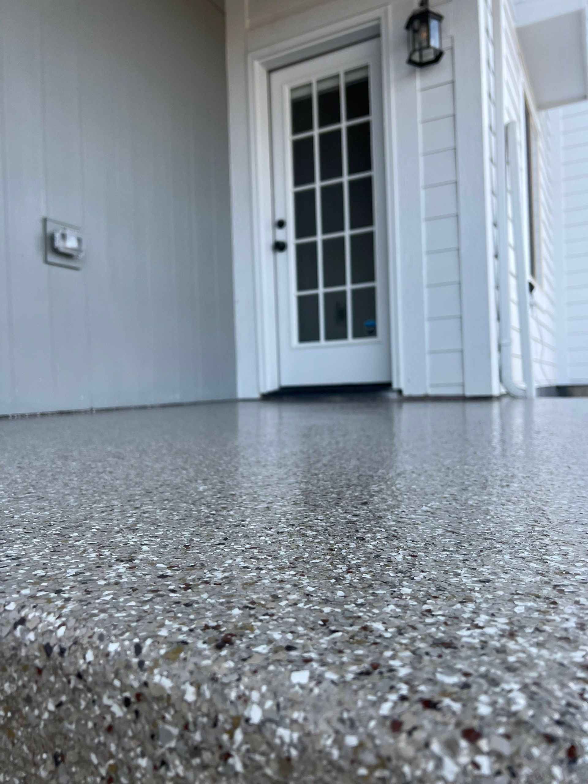 Porch with speckled concrete floor and a white glass-paneled front door.