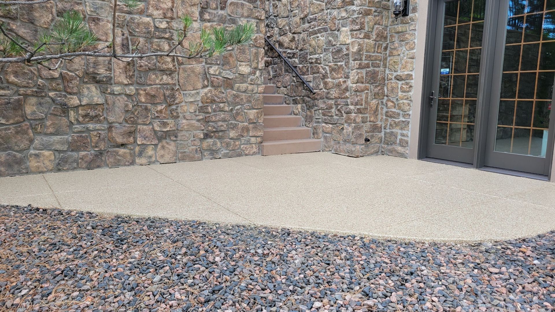 Stone wall courtyard with gravel ground, a small concrete area, steps, and glass doors on the right