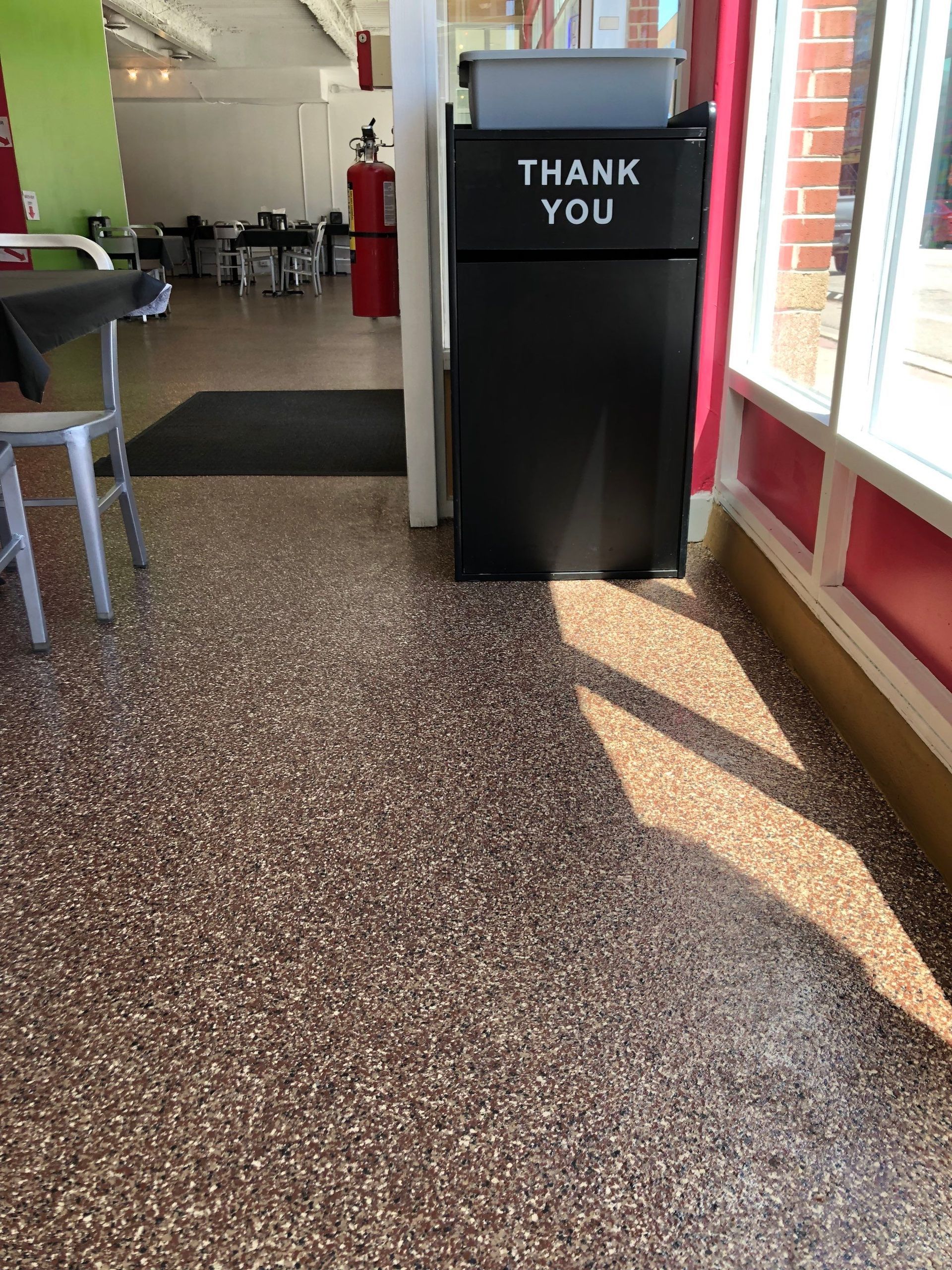 Black “THANK YOU” trash bin in a sunlit diner hallway with red walls and speckled floor