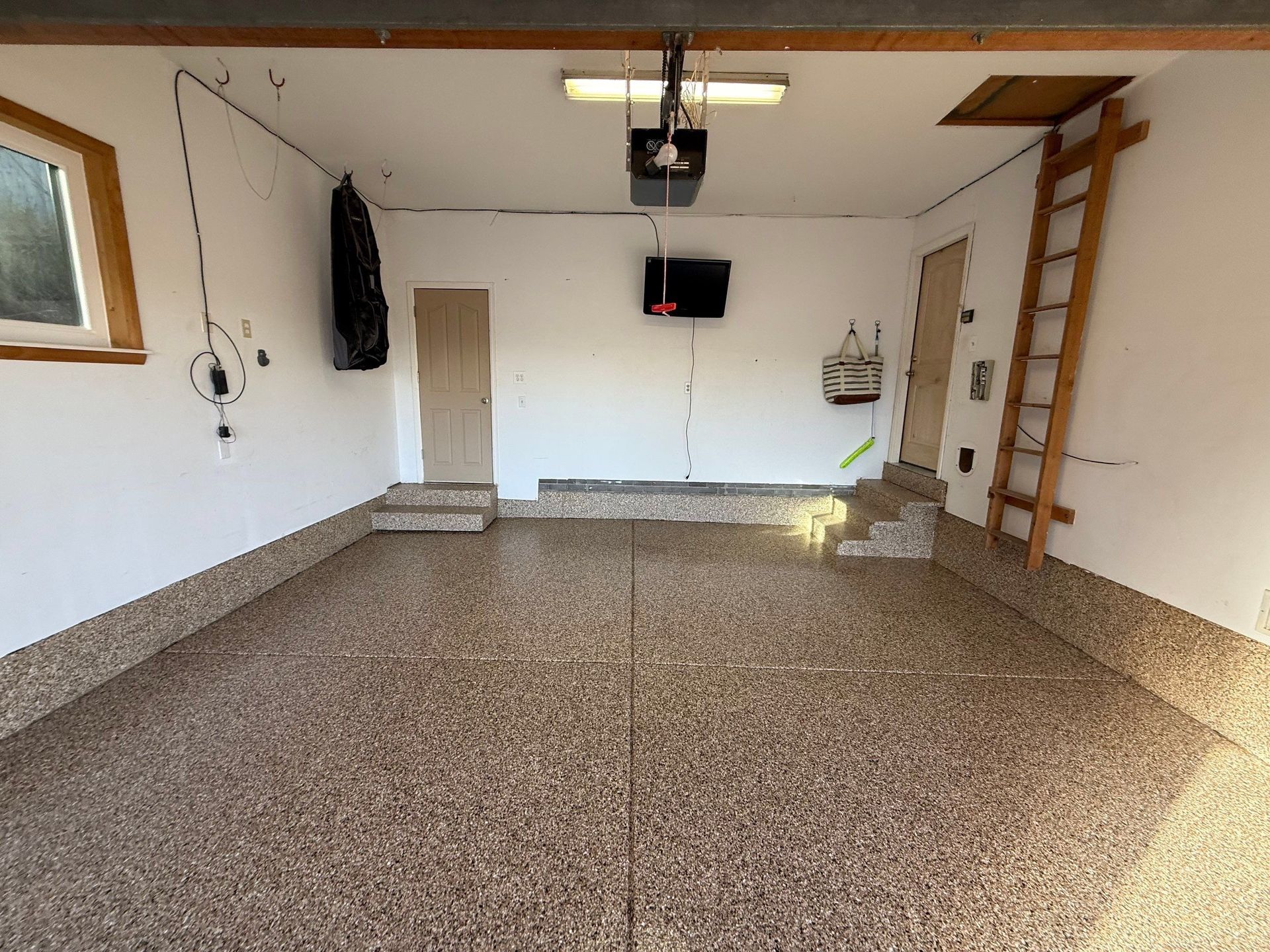 Empty garage with speckled floor, white walls, ceiling lift, and wooden ladder on the right.
