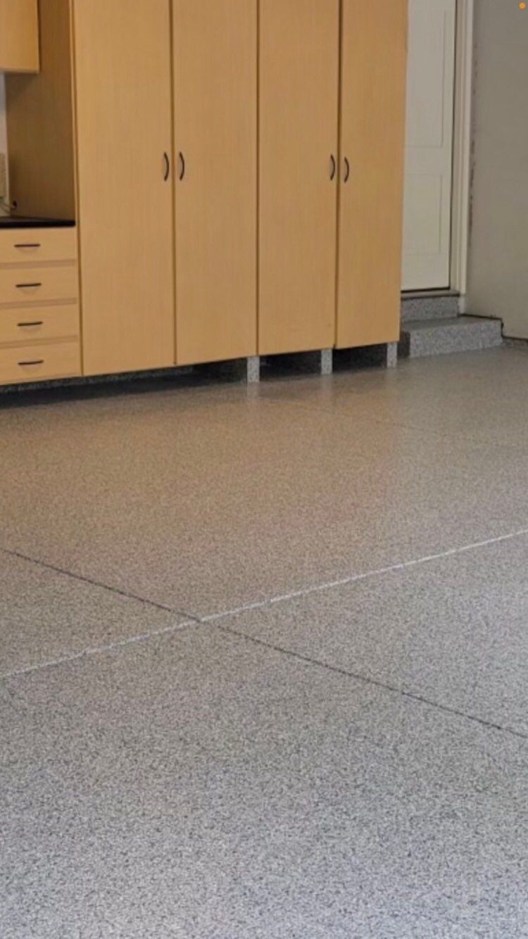 Speckled floor in a room with light wood cabinets and a closed door in the background