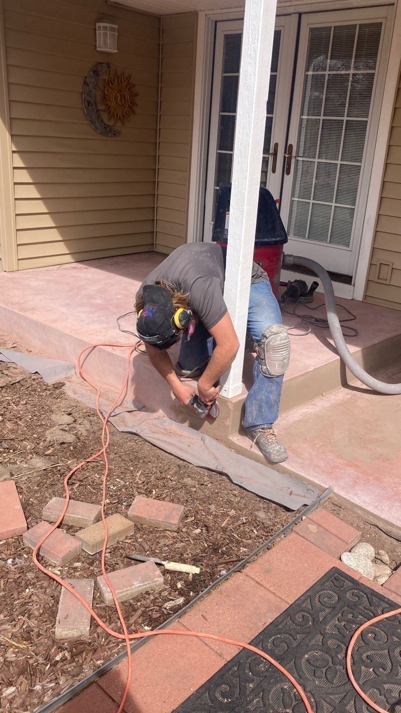 Worker kneeling on a front porch, smoothing wet concrete near the steps and doorway.