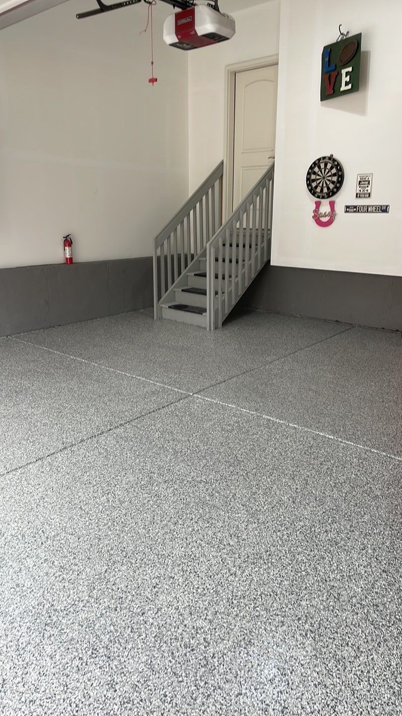 Empty garage with speckled gray floor, white walls, and a small gray staircase leading to a door.