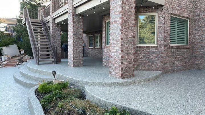 Brick house patio with curved concrete steps, metal stairs, and windows under an elevated deck