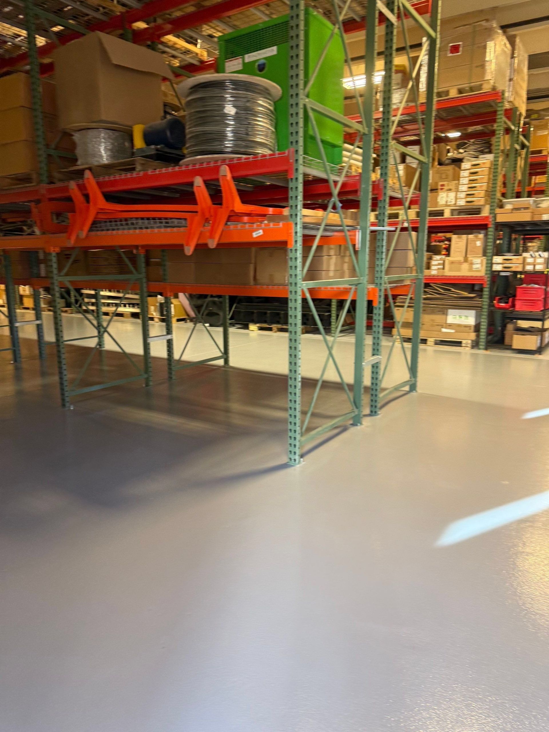 Warehouse aisle with metal racks, orange shelving, and stacked boxes under bright industrial lighting