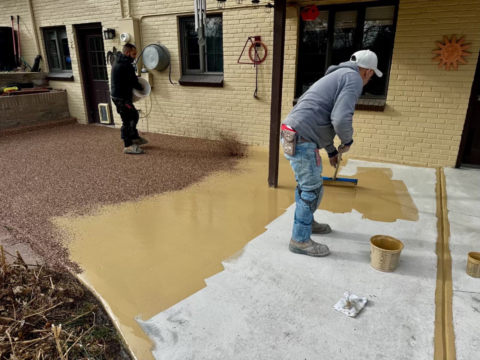 Two workers painting a brick patio and walkway with tan and white coatings