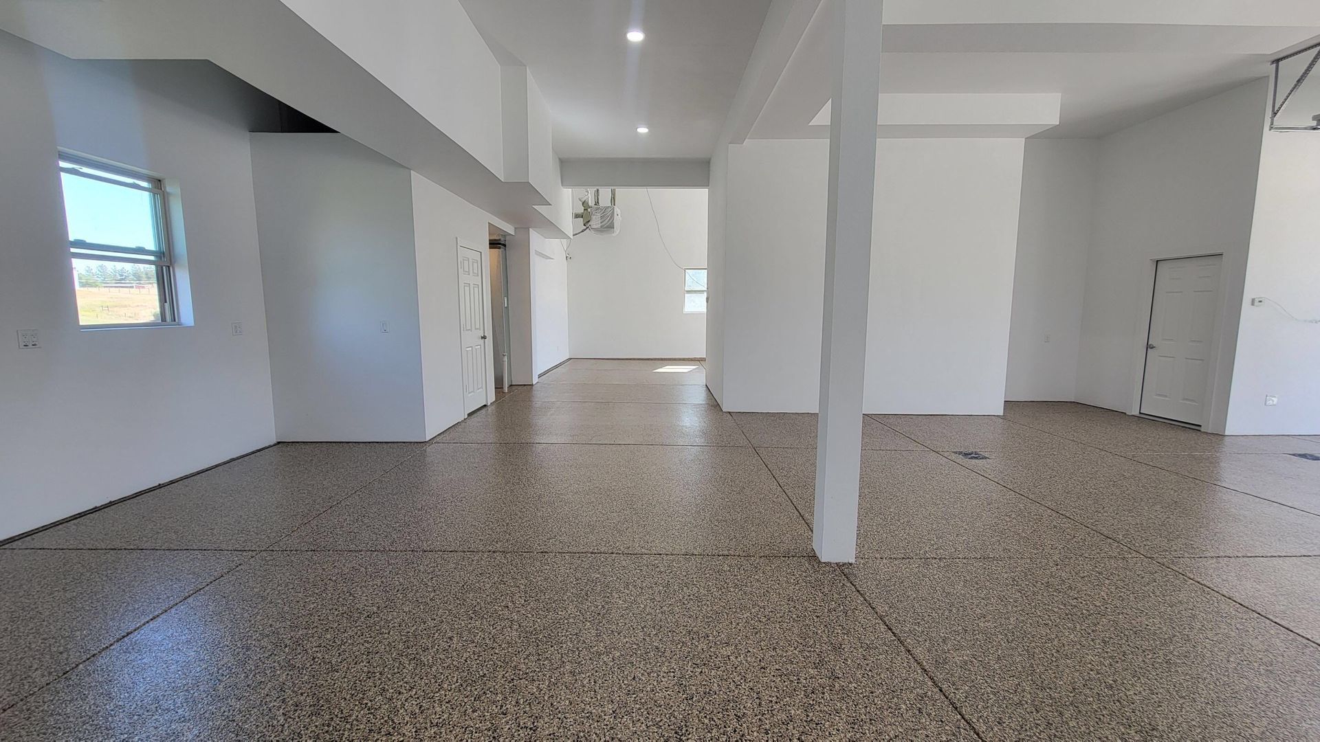 Empty white room with terrazzo floor, support columns, windows, and recessed ceiling lights.