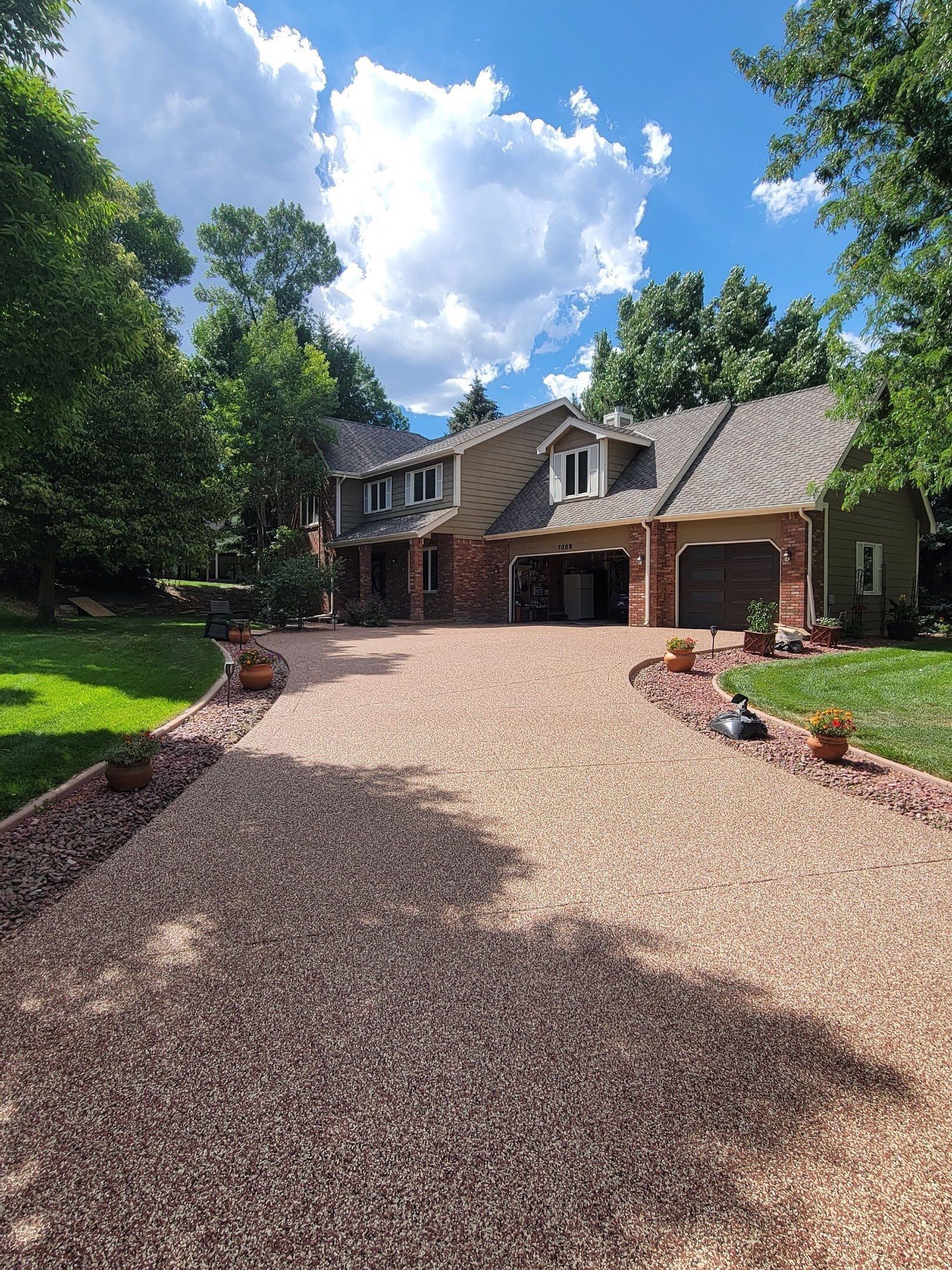 Large brick house with a gravel driveway and trees on a sunny day