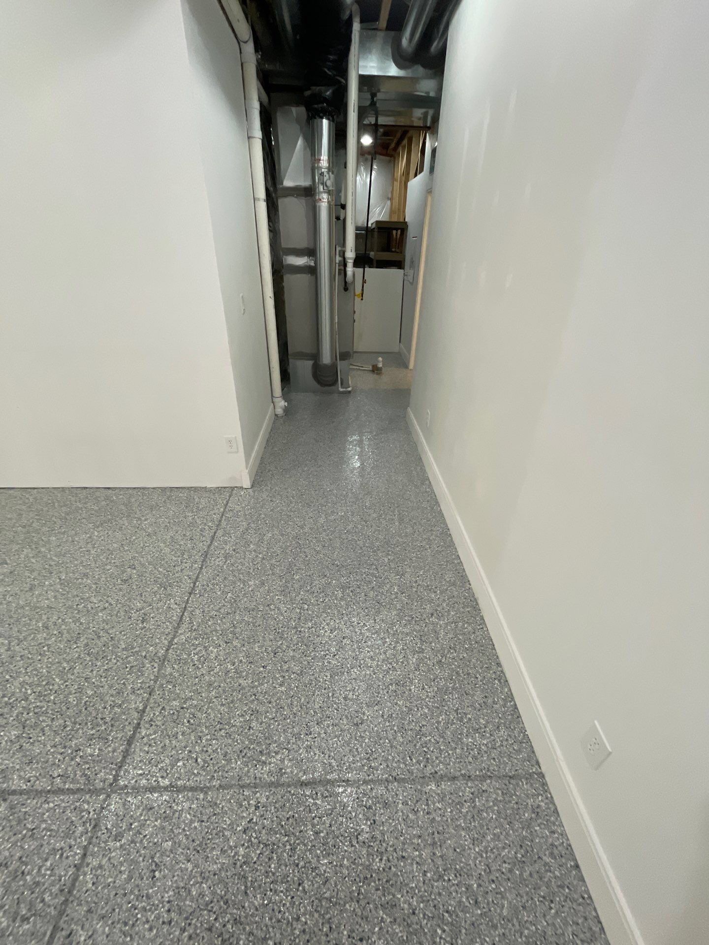 Narrow hallway with white walls, speckled gray floor, and exposed pipes at the far end.