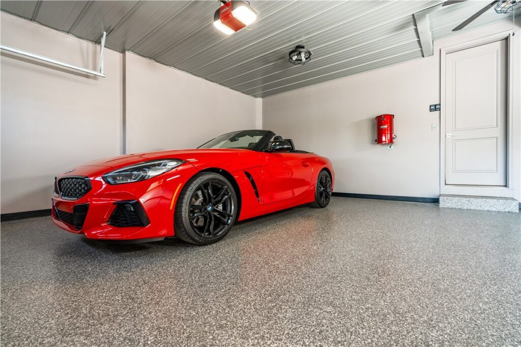 Red sports car parked in a clean garage with white walls and gray speckled floor