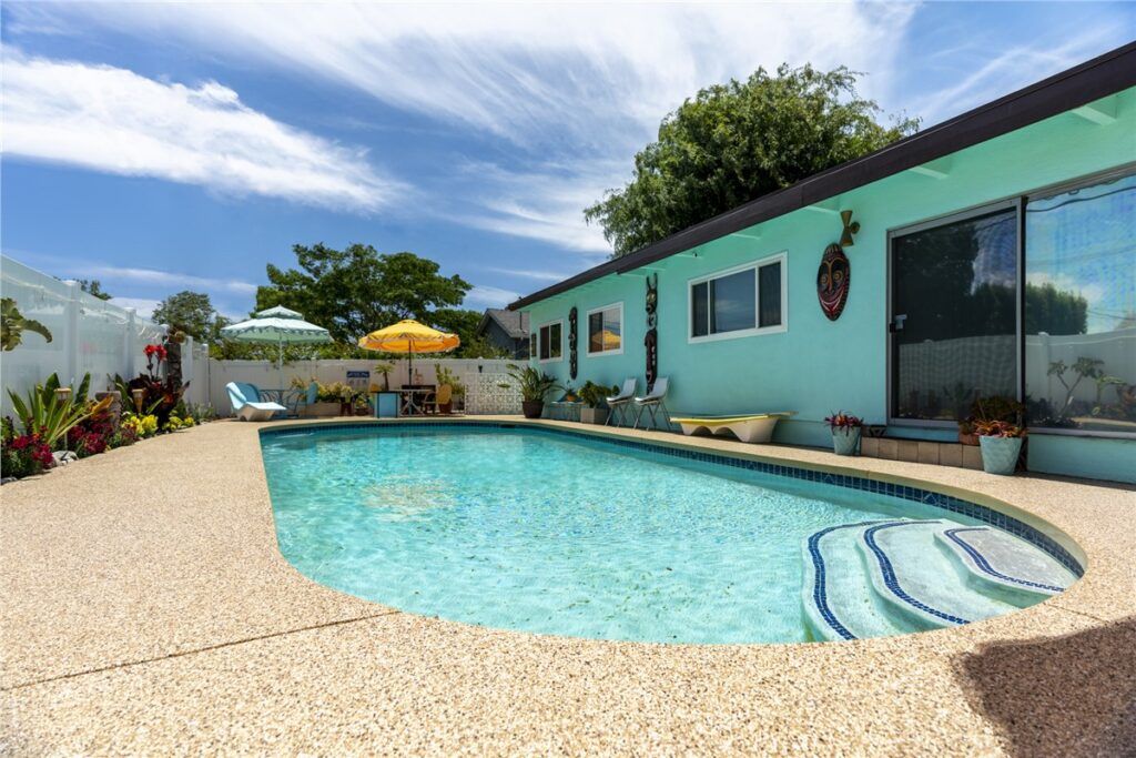 Turquoise pool beside a aqua house with patio and lounge chairs on a sunny day