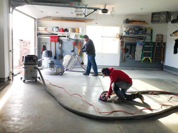 Workers grinding a concrete garage floor with power tools and hoses