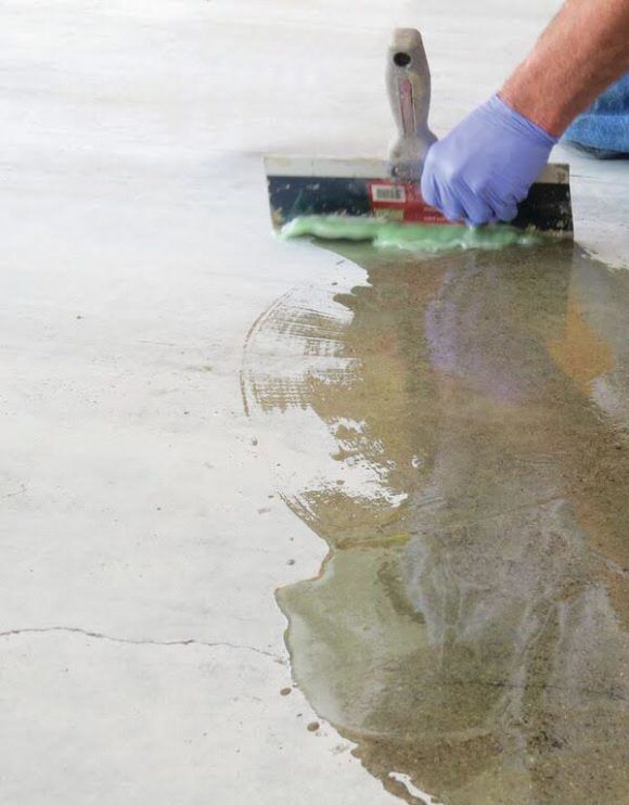 Gloved worker smoothing wet concrete with a trowel on a floor surface