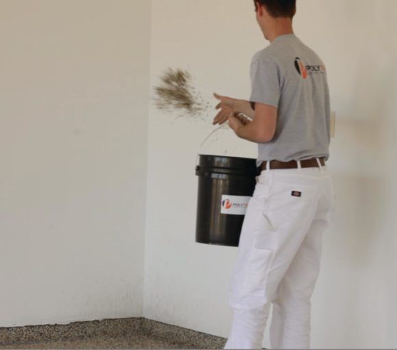 Person using a black bucket to spray or clean a white wall indoors