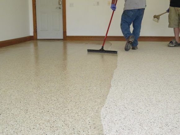 People mopping a shiny floor in a room with a white wall and door.