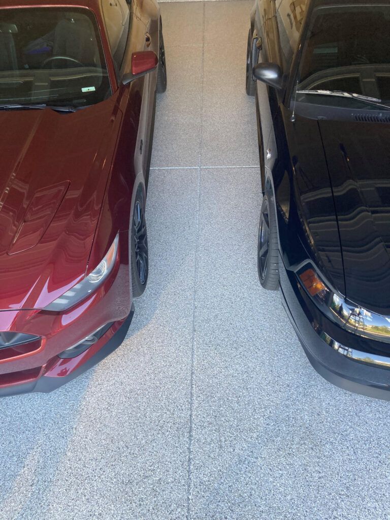 Two cars parked side by side in a narrow garage, one red and one black.