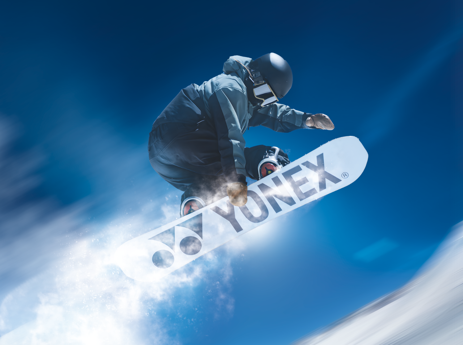 Snowboarder in der Luft, auf einem YONEX-Board vor strahlend blauem Himmel.