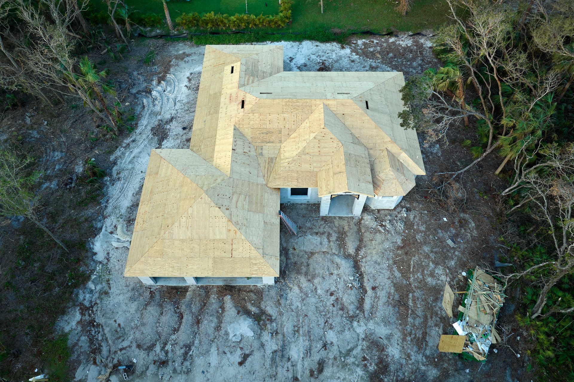 Aerial view of a house under construction with exposed wooden framing and bare ground around it.