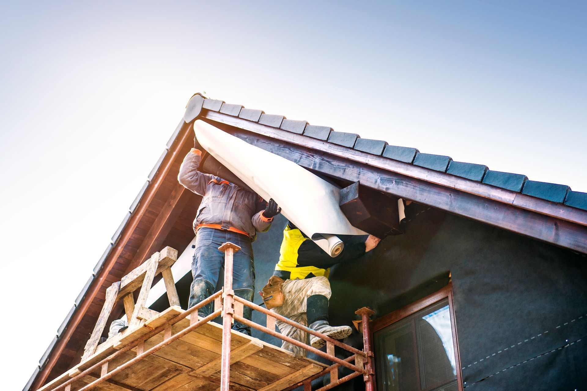 Workers on scaffolding installing roof trim on a house under construction