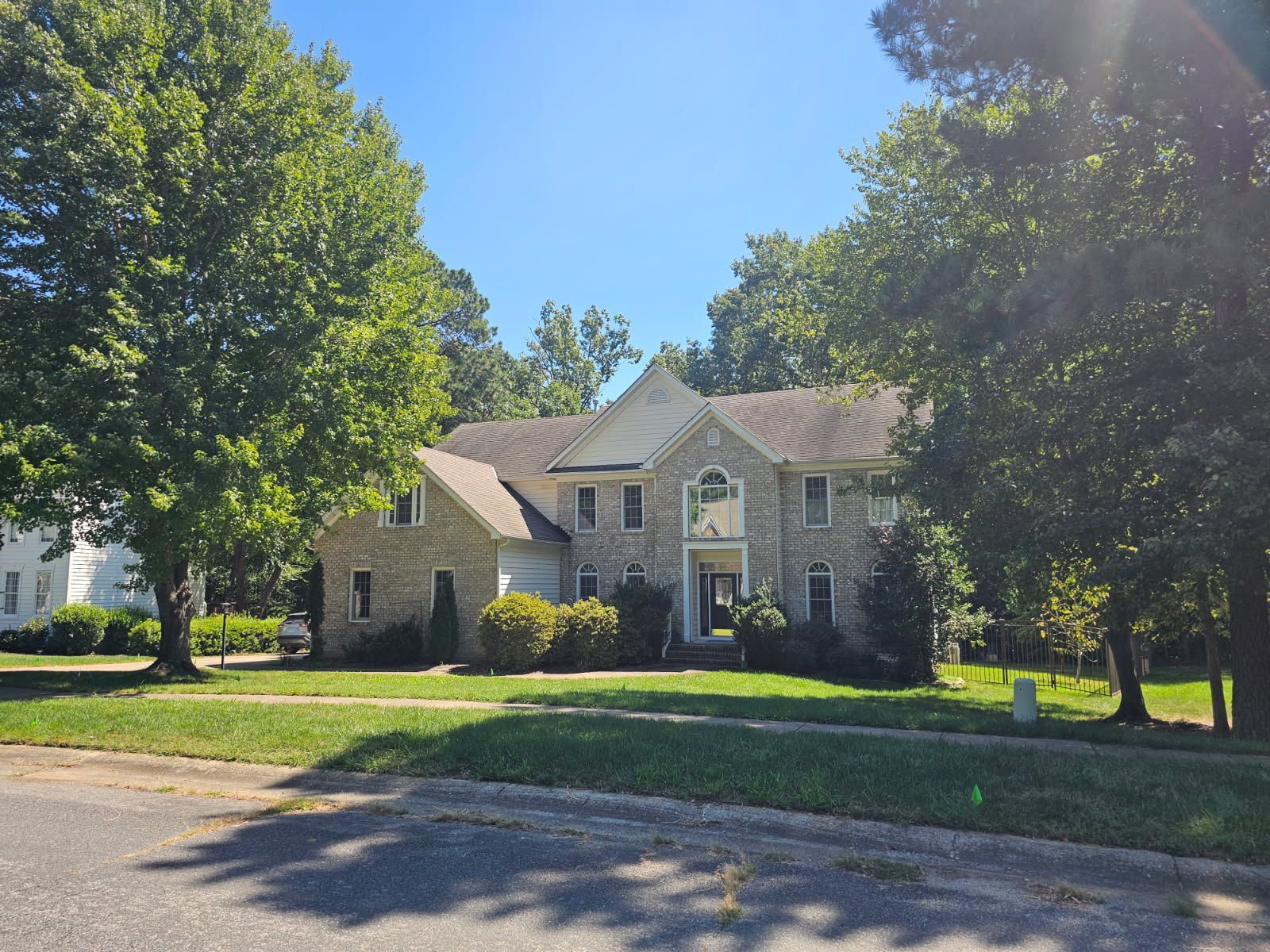 A two-story brick residential home featuring a recently installed roof with multiple gable sections and asphalt shingles by D & B Roofing Services