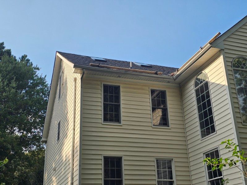 A two-story residential home with visible roof damage and deterioration along the roofline and shingles requiring repair by D & B Roofing Services