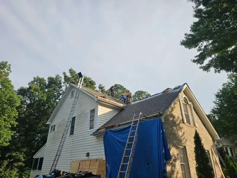 A residential roof replacement in progress with protective tarping and staging ladders positioned on both the front and side