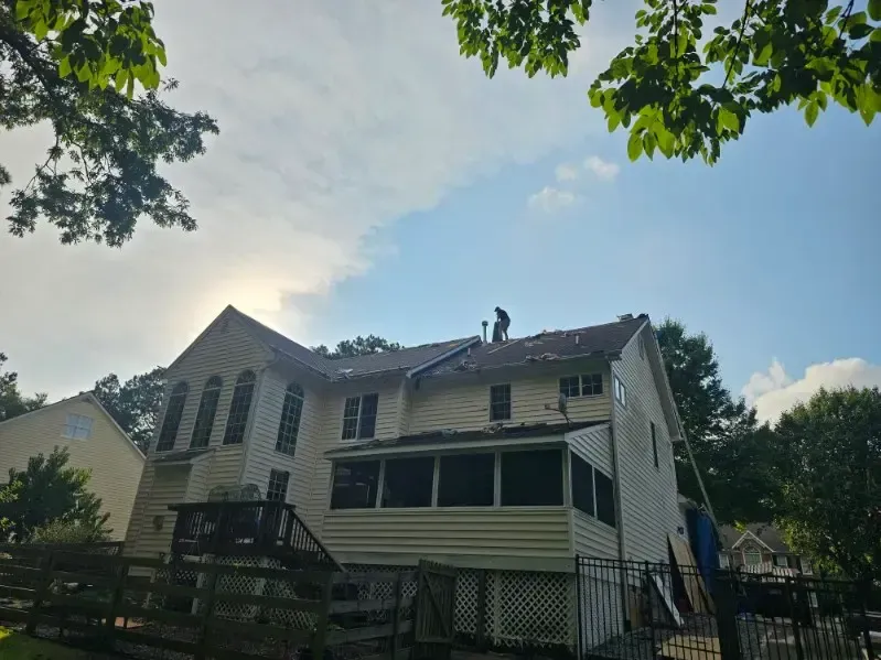 A two-story residential home with roof work in progress, showing workers on the roof during an active roofing project by D & B Services
