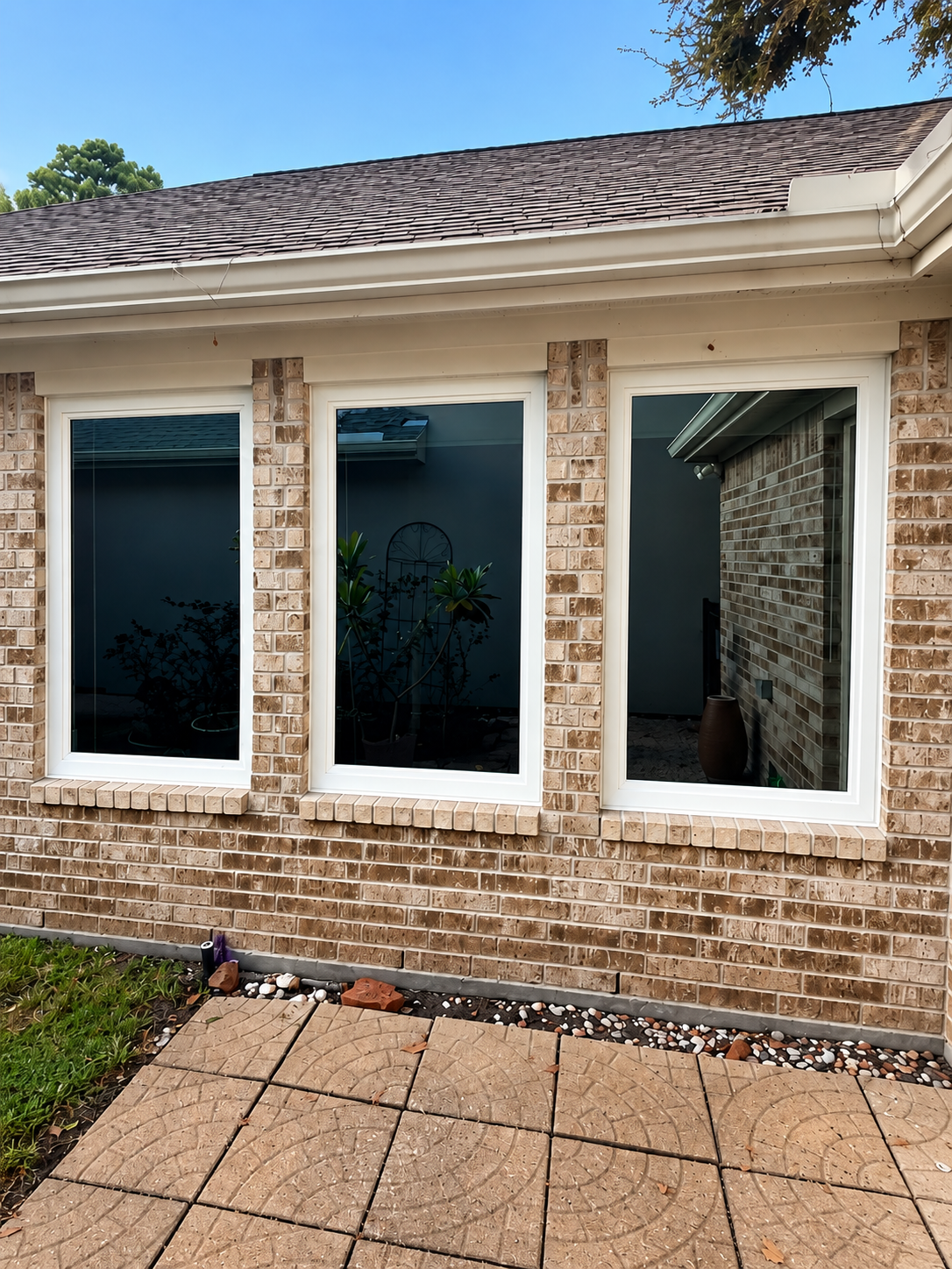 Brick house exterior with three dark-tinted windows and a small tiled patio in front