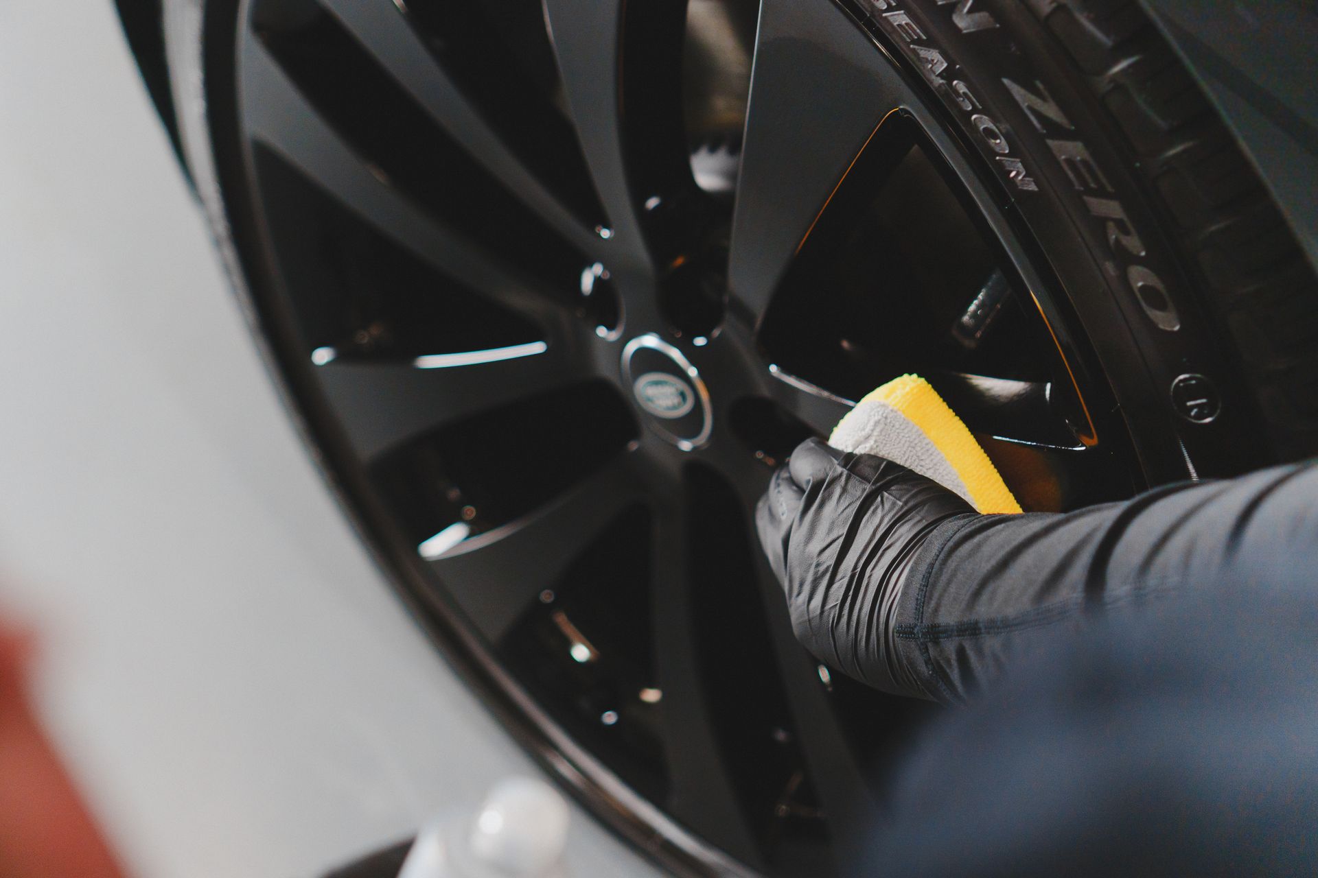A person is cleaning a car wheel with a yellow sponge.