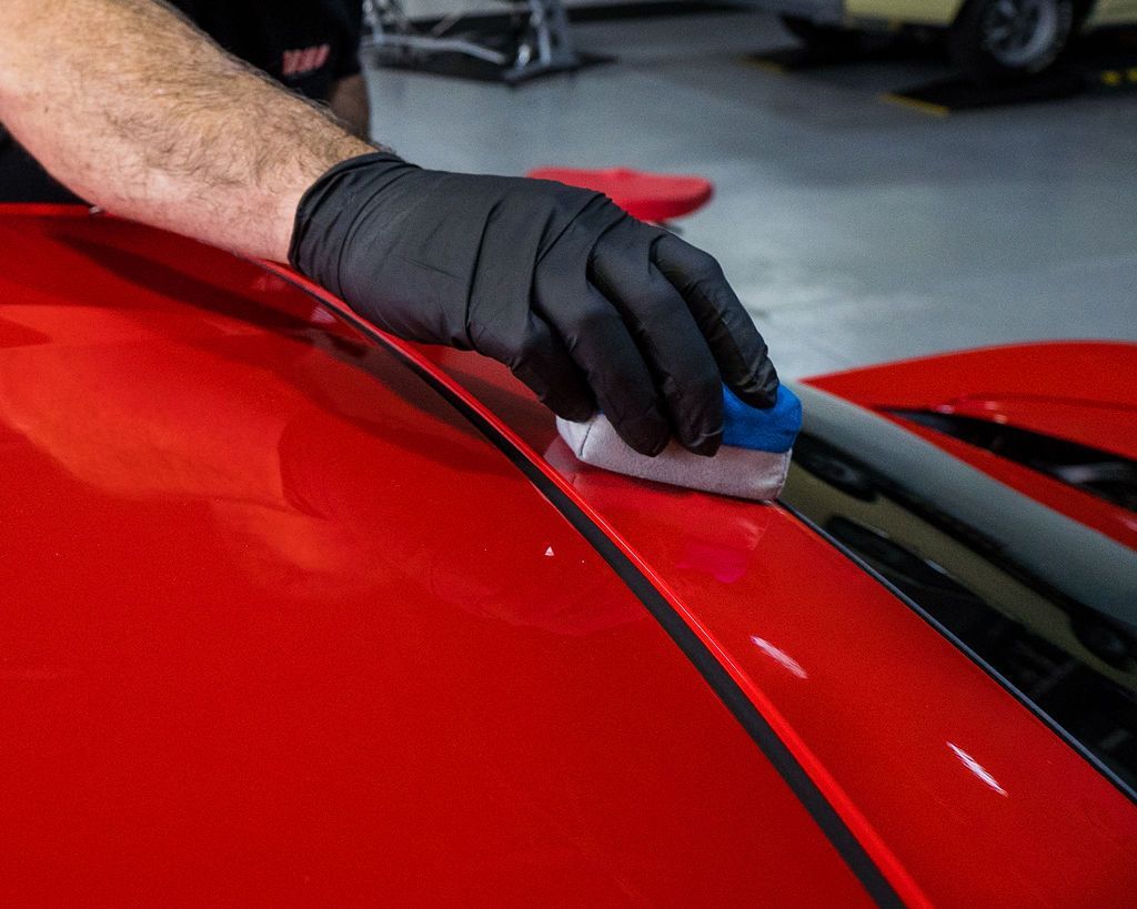 A person is polishing a red car with a sponge.