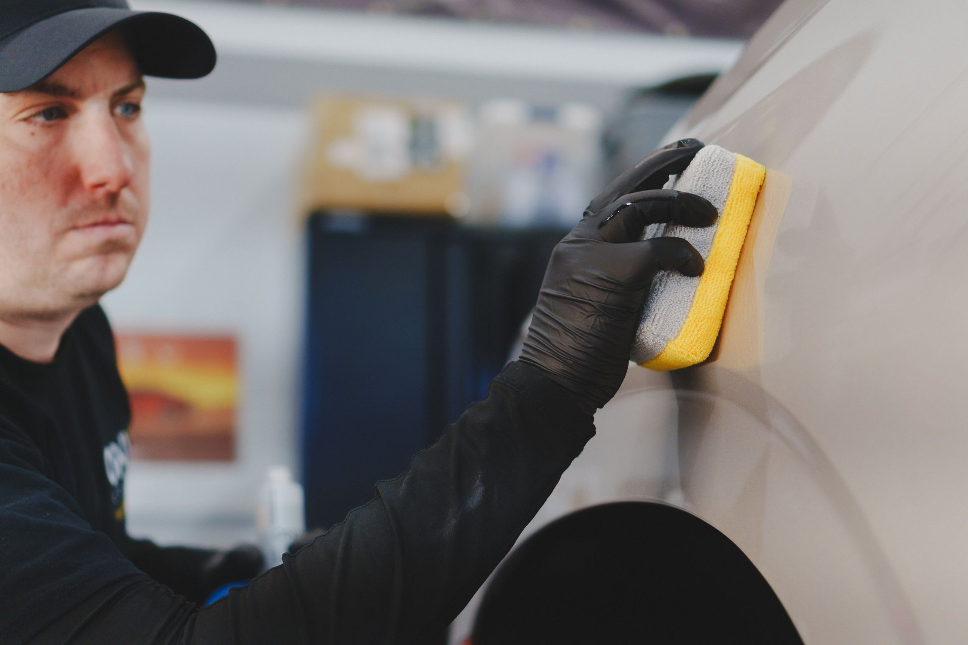 Mechanic polishing a silver car with a yellow sponge and black gloves