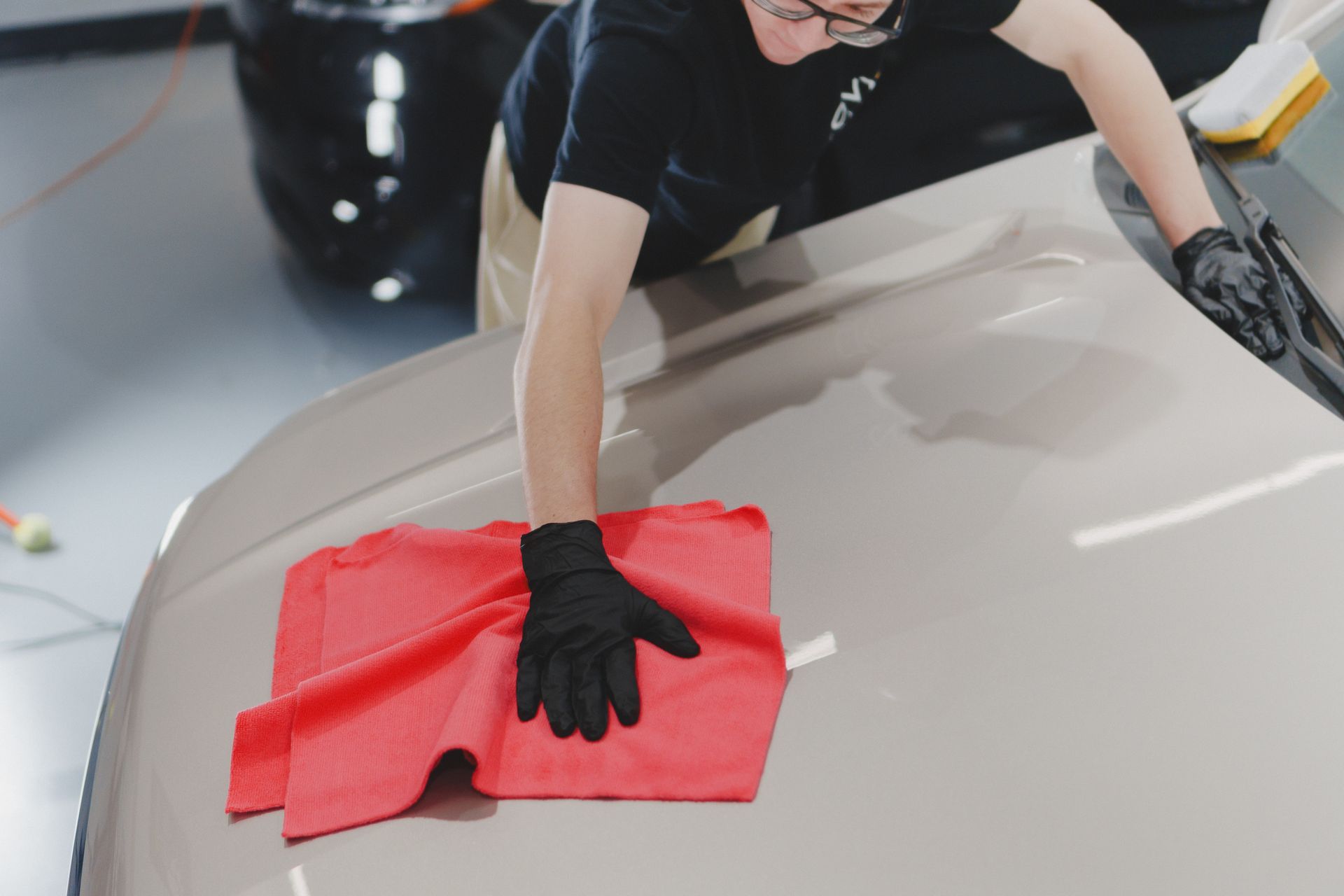 Person cleaning a car hood with a red cloth and black gloves
