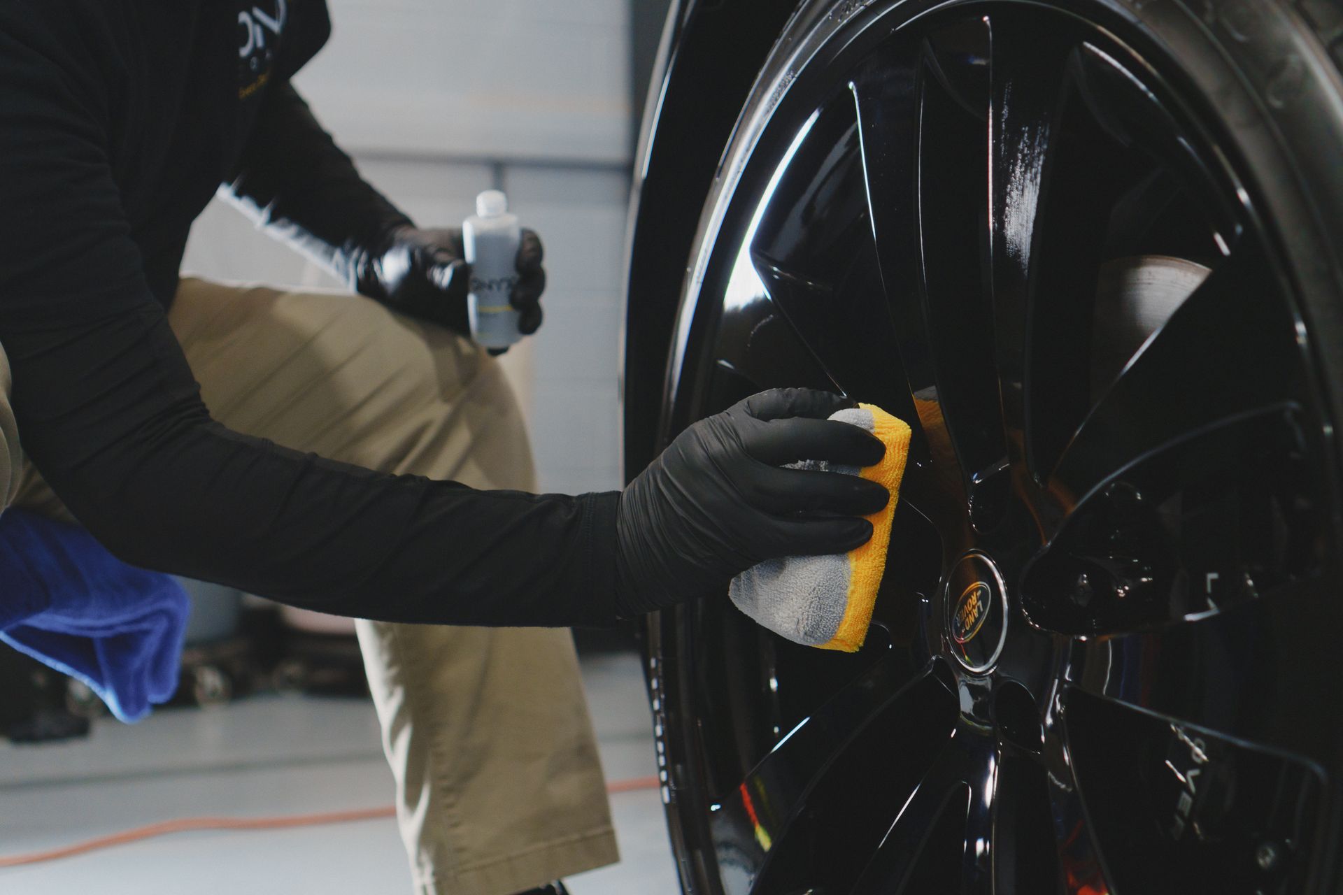 A man is cleaning a car wheel with a yellow sponge.