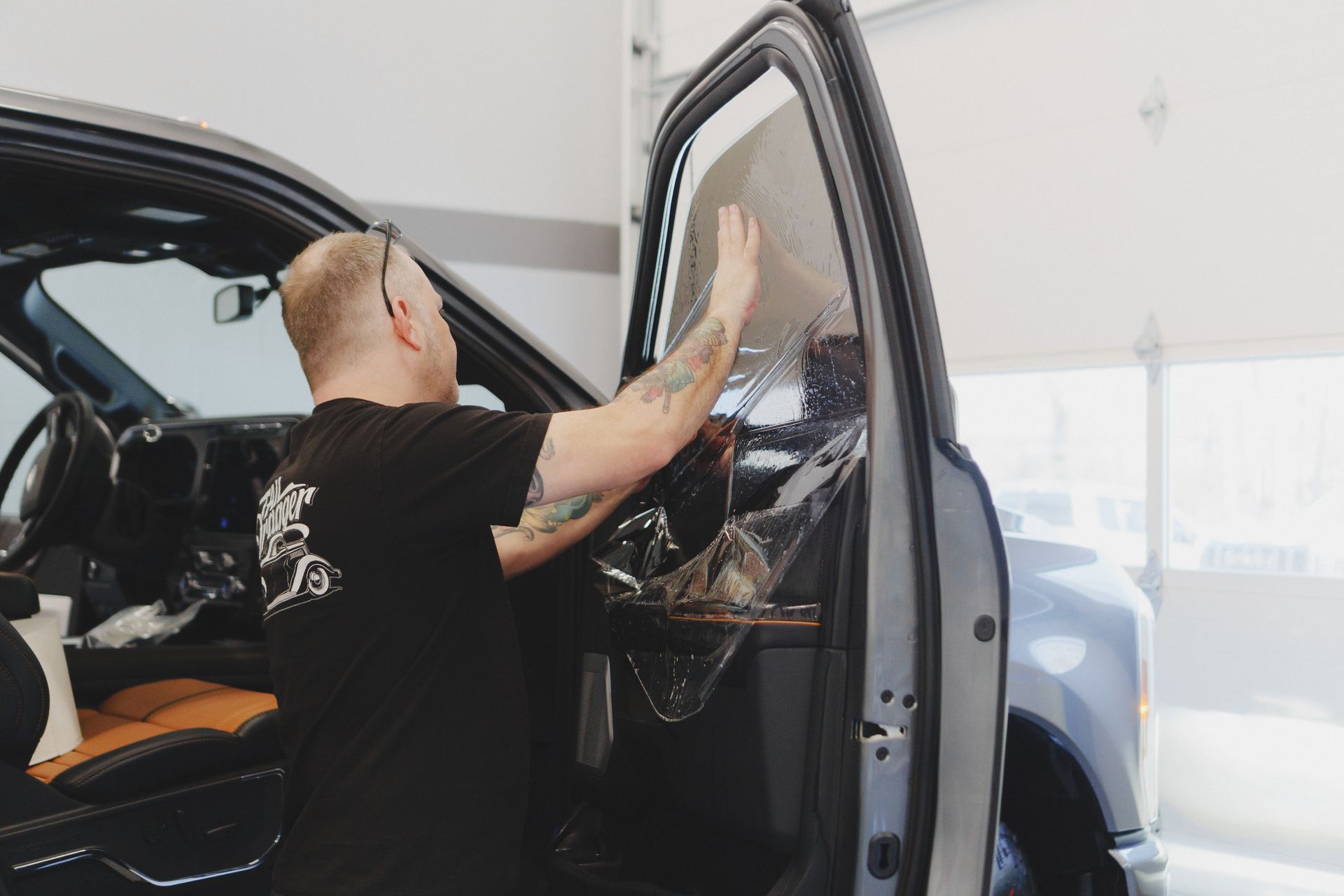 Man applying tint to a car window inside a shop.