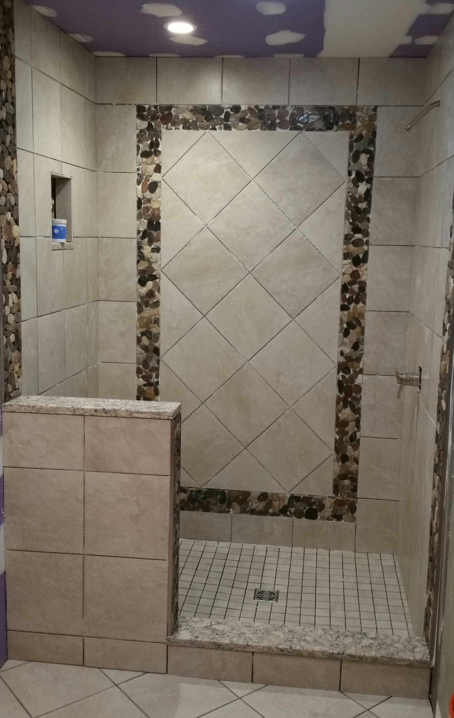 A walk-in shower with neutral square tiles, a central diamond-patterned accent wall, and stone border detailing.