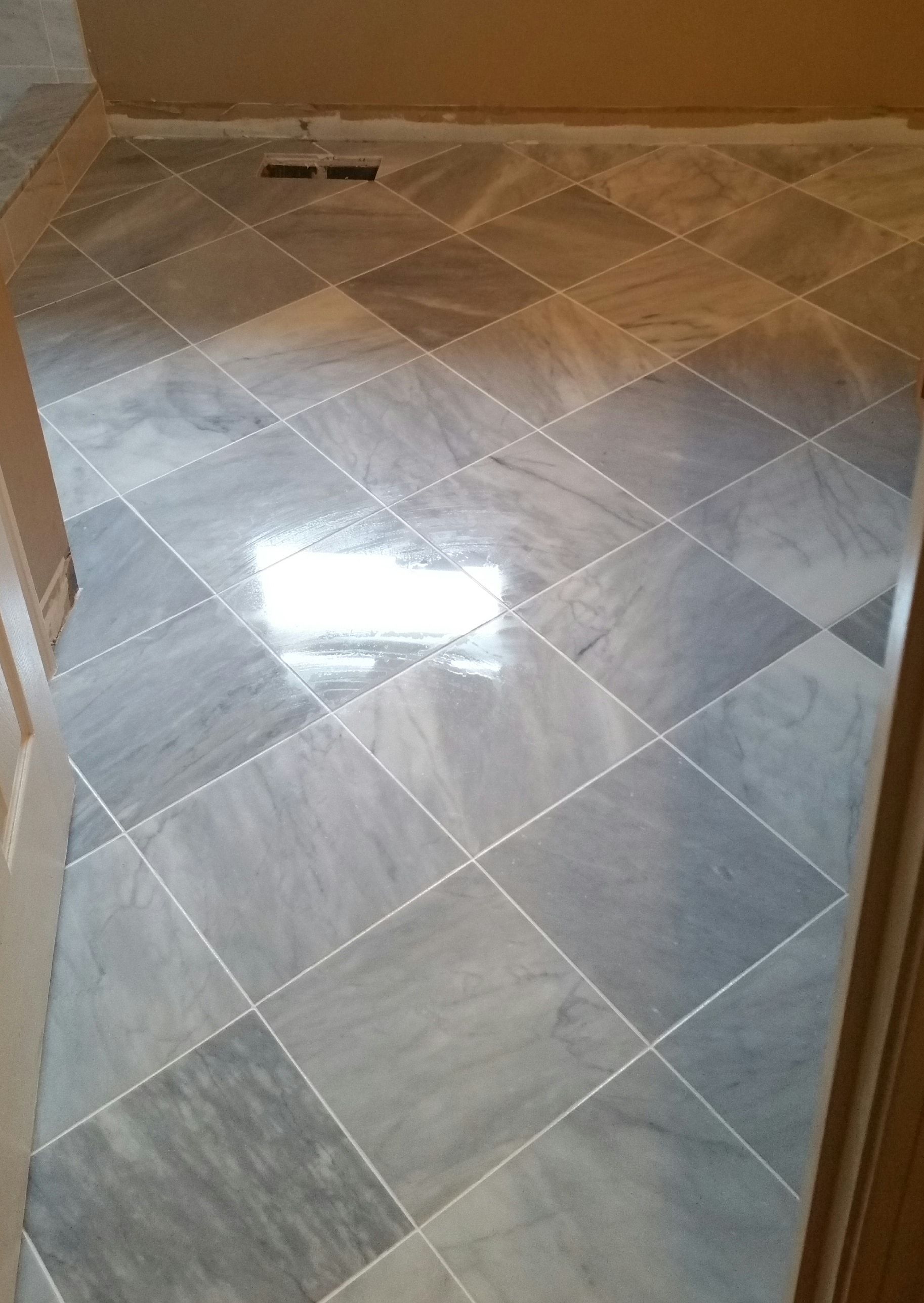 A floor covered in gray and white marbled square tiles laid in a diamond pattern, featuring a centered vent.
