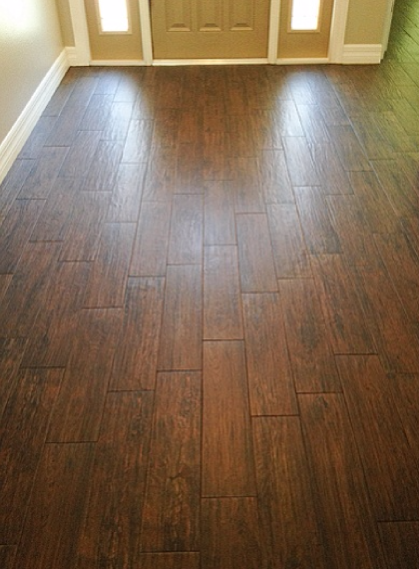 Dark brown wood-look tile flooring in a hallway leading to a front door with sidelights.