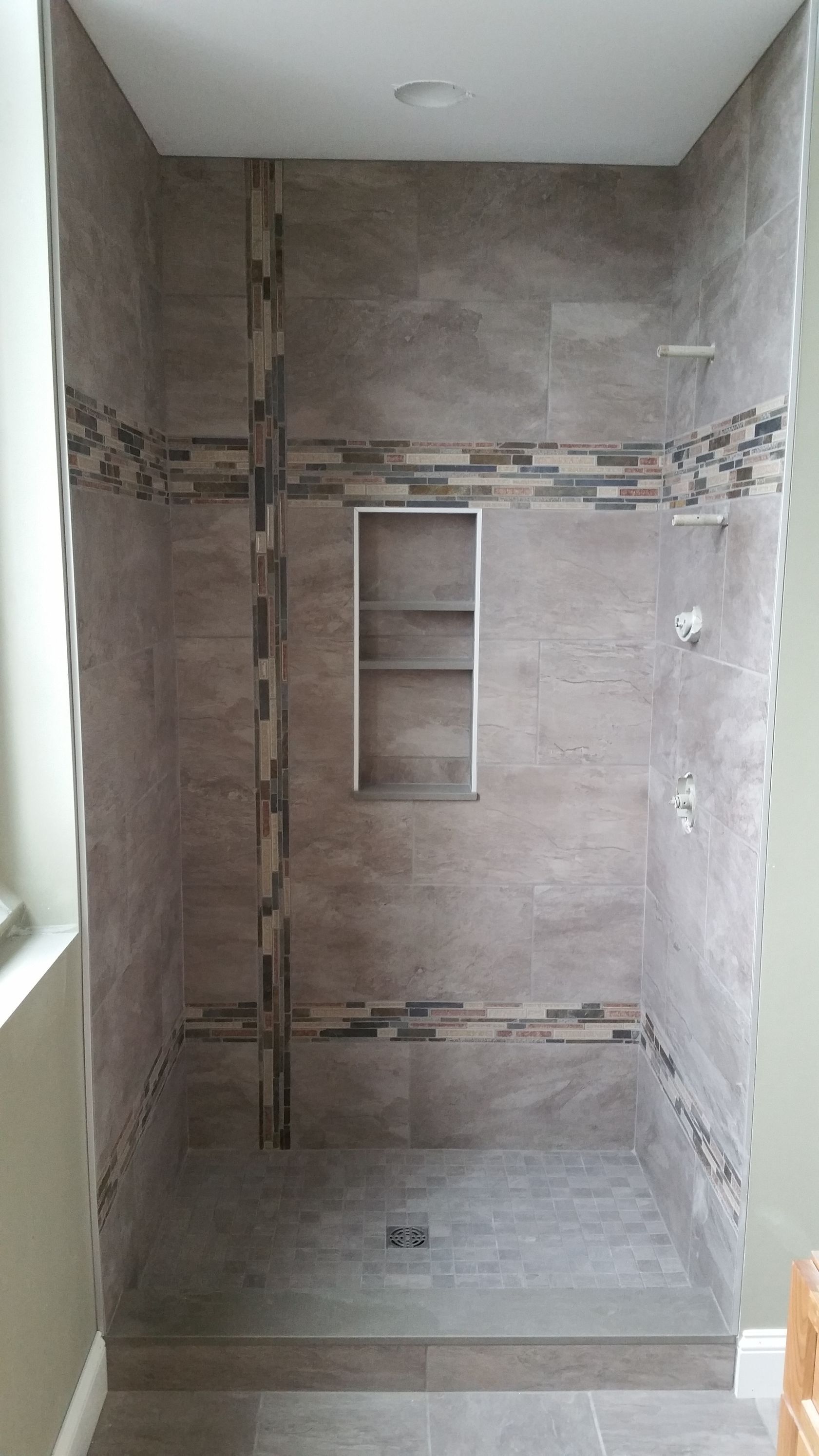 A walk-in shower with grey tiles, a central vertical mosaic strip, a recessed niche, and a tiled curb.