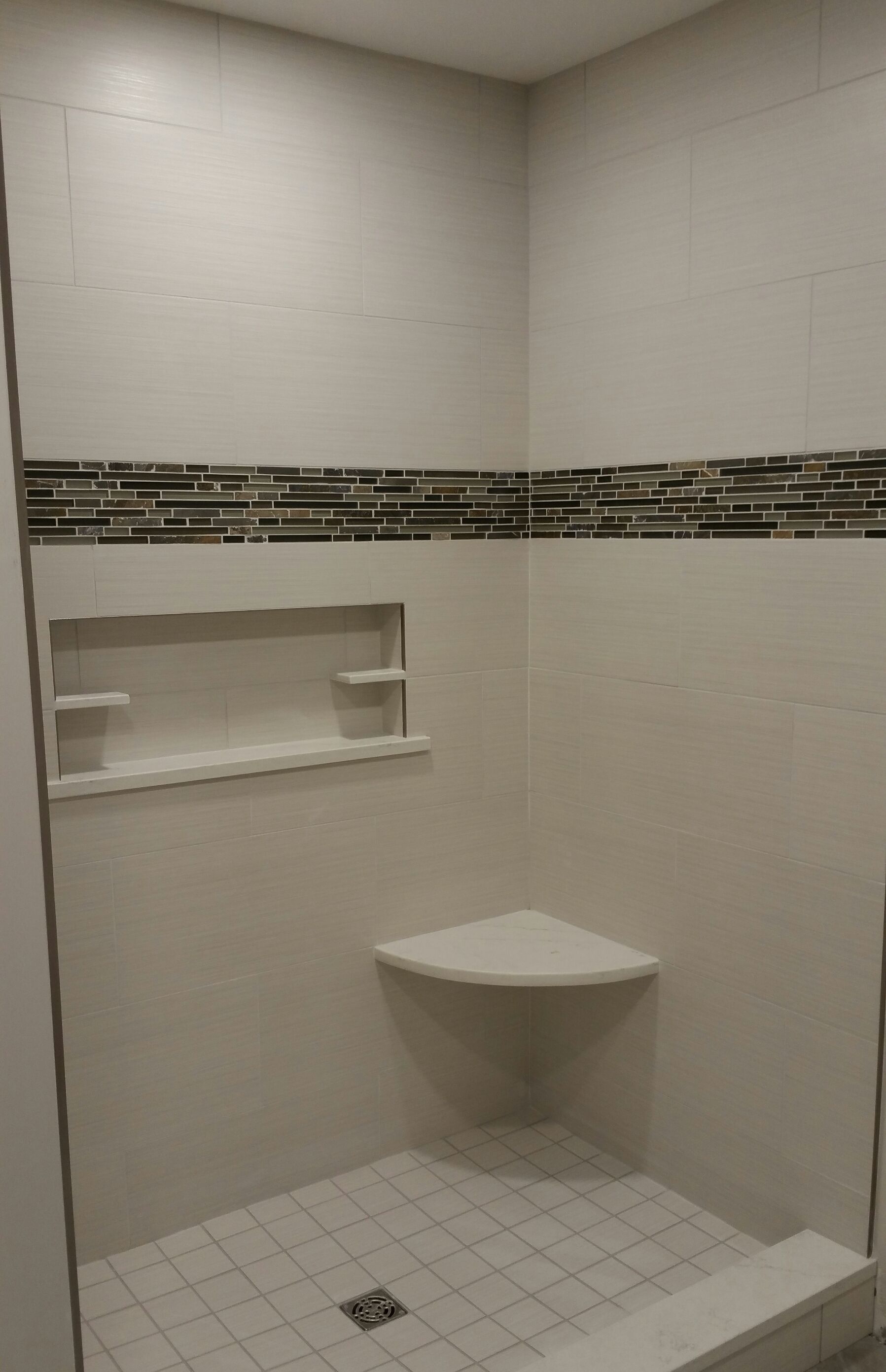 A tiled shower stall with a corner bench, a recessed wall niche for toiletries, and a decorative horizontal mosaic tile.