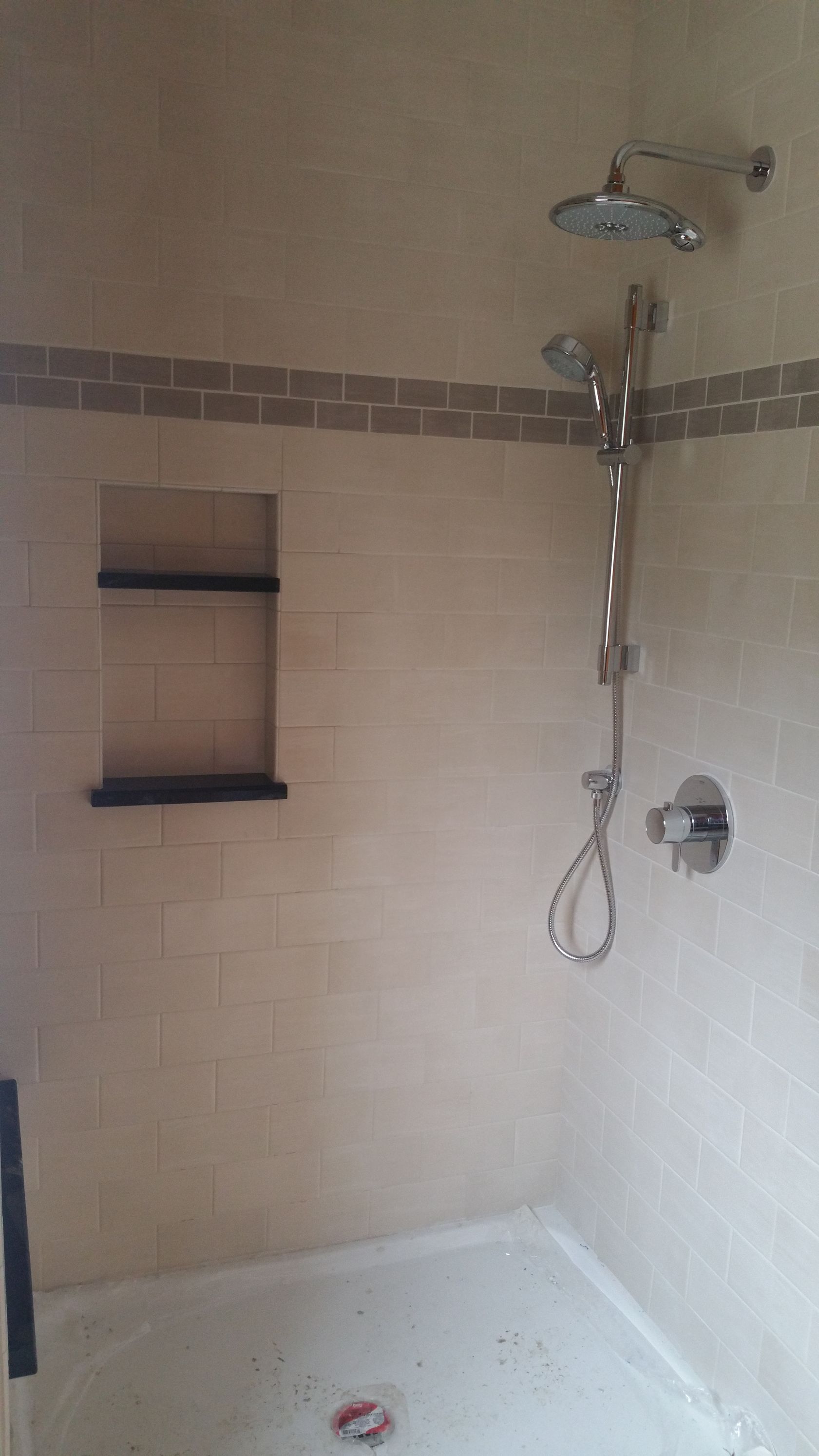 A walk-in shower with beige subway-tiled walls, a built-in recessed shelf, a dual showerhead system, and a white shower pan.